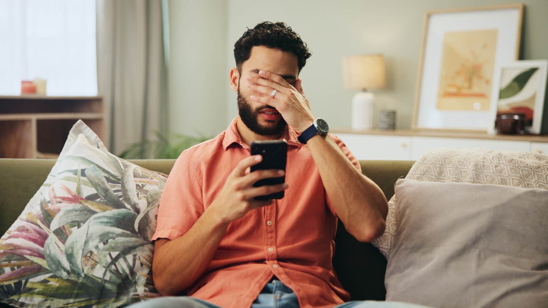 upset man rubbing his face while holding phone