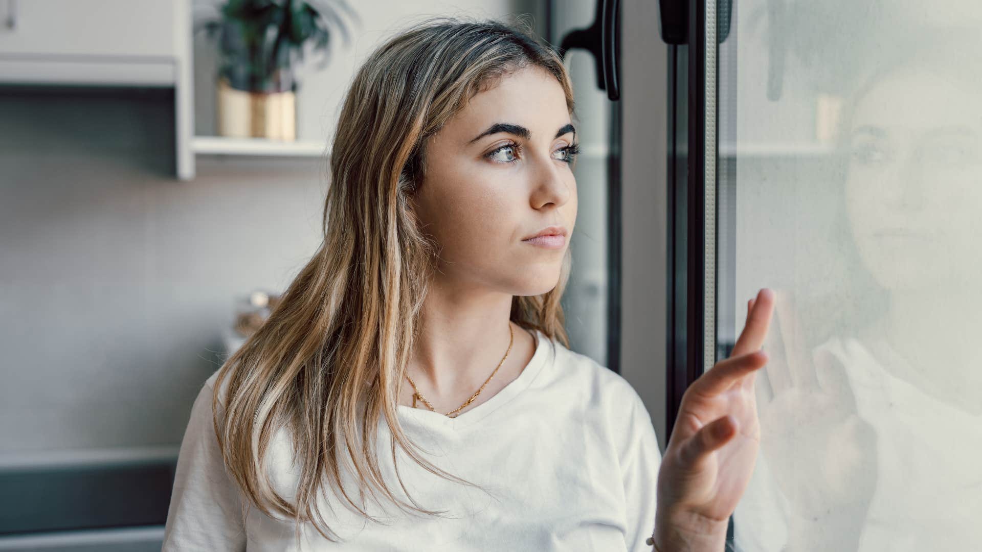 Uncertain person looks out window showing attempt to understand trauma