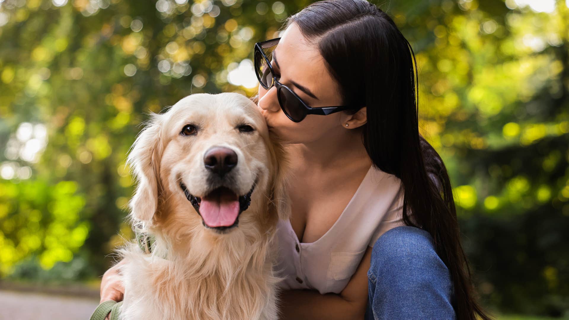 woman kissing golden retriever's head outside