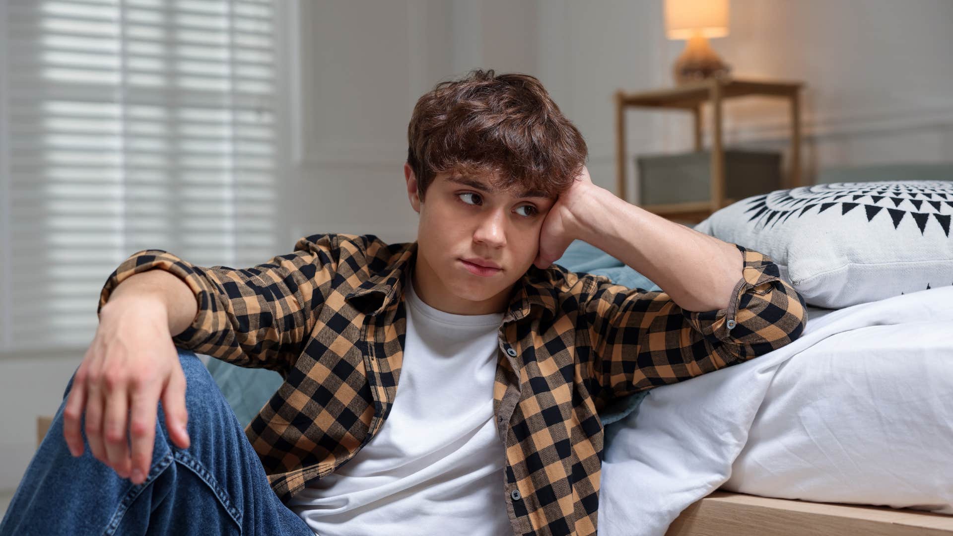 upset teen boy sitting on floor in bedroom