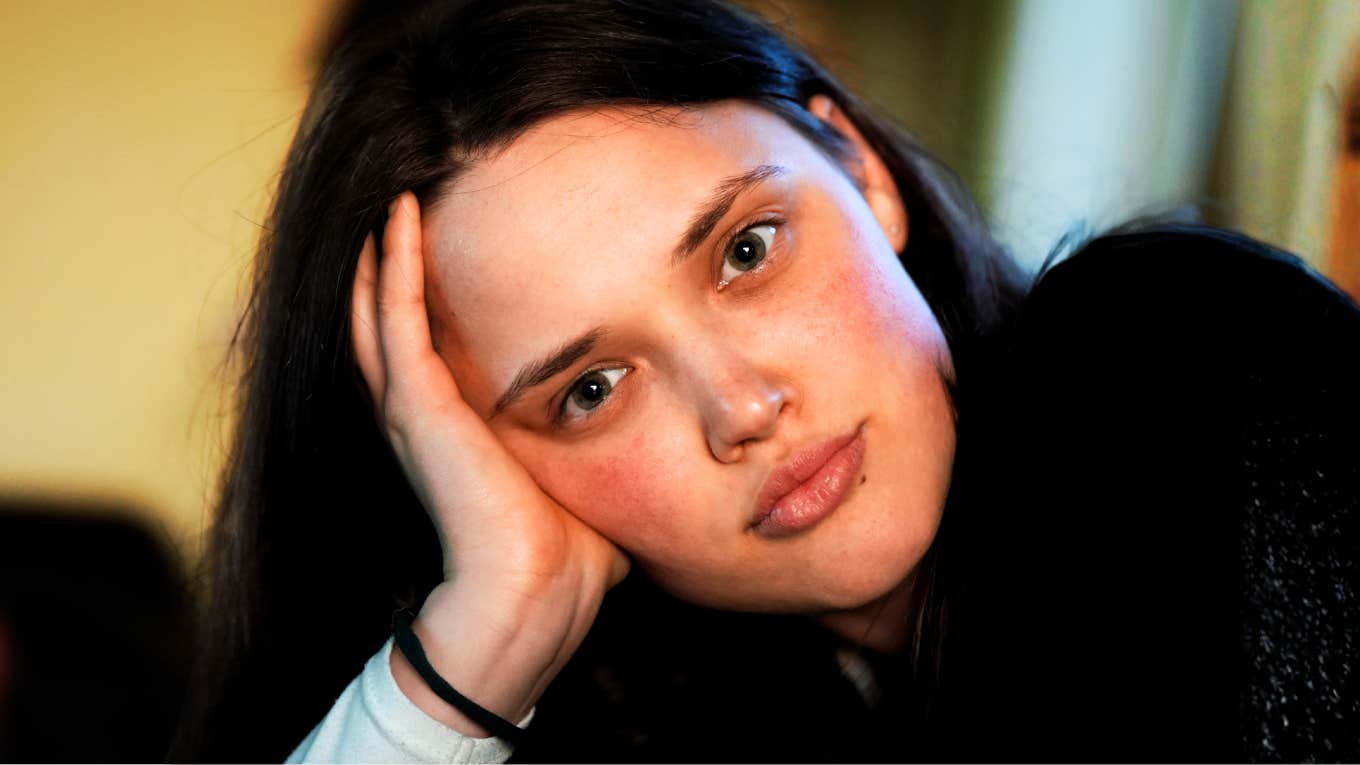 A woman with dark hair resting her head on her hand inside a room.