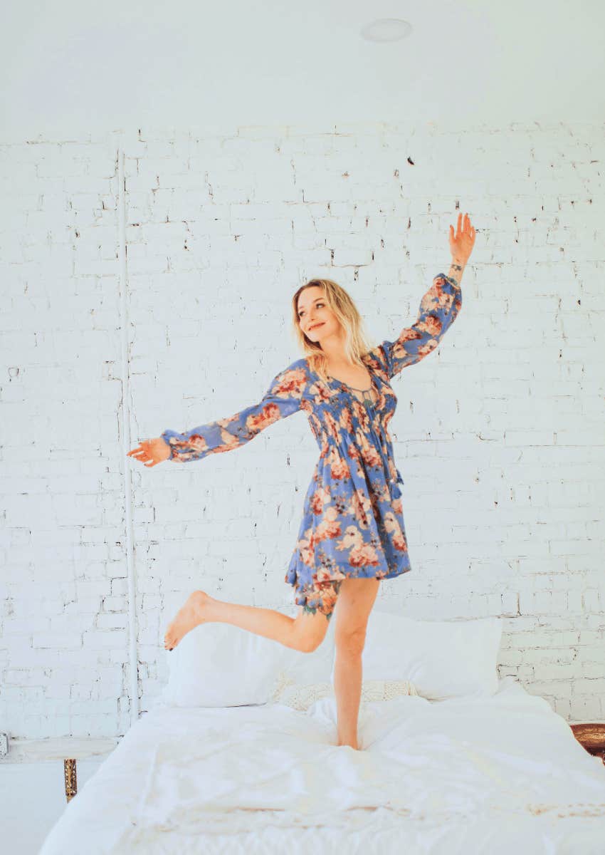 happy woman standing on her bed wearing a dress