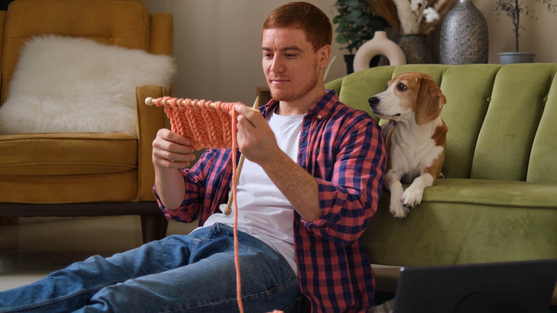 man crocheting at home next to his dog