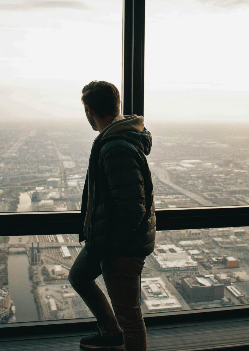 man looking out of window at city view