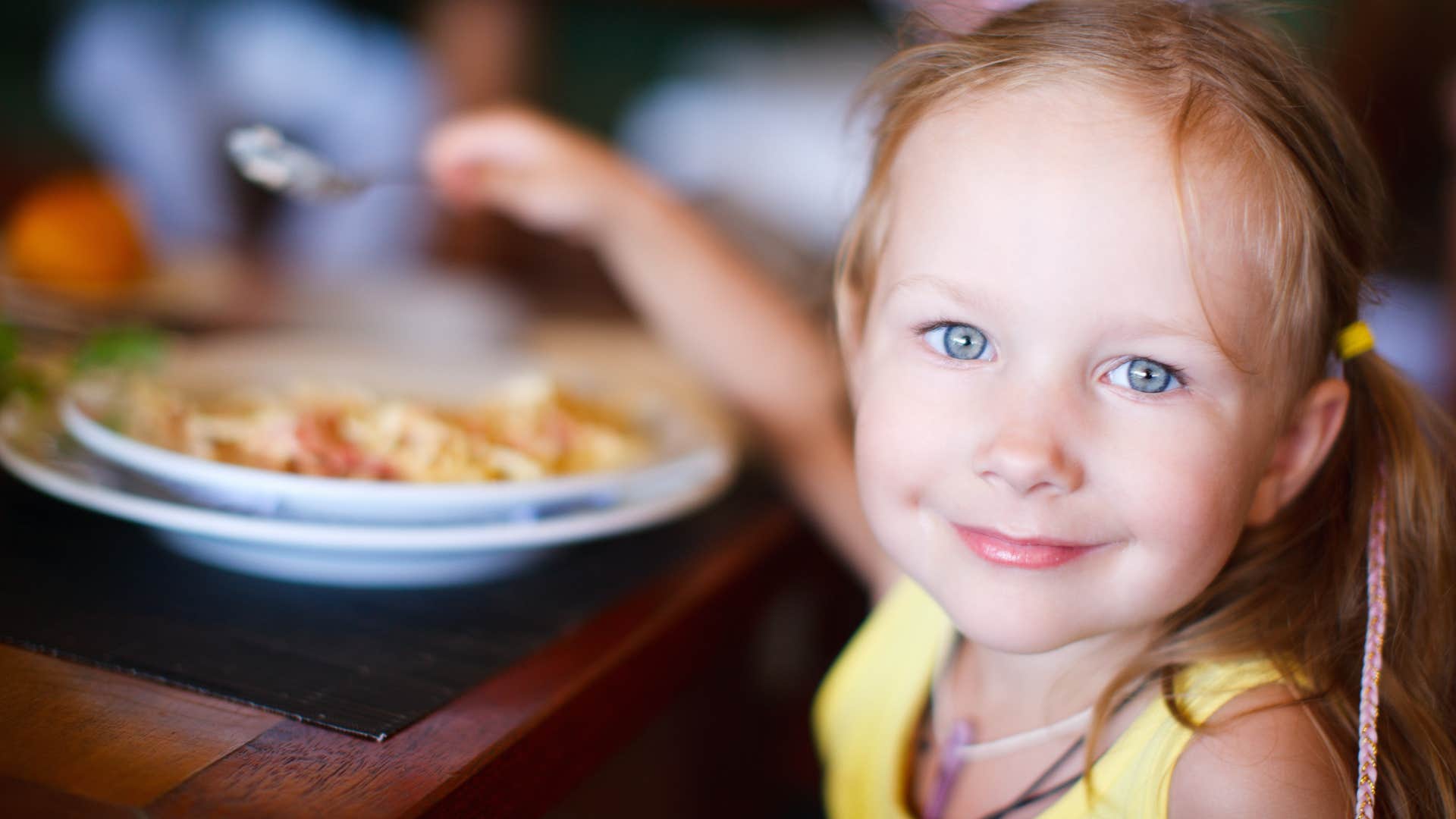 little girl at dinner with her parents eating and smiling
