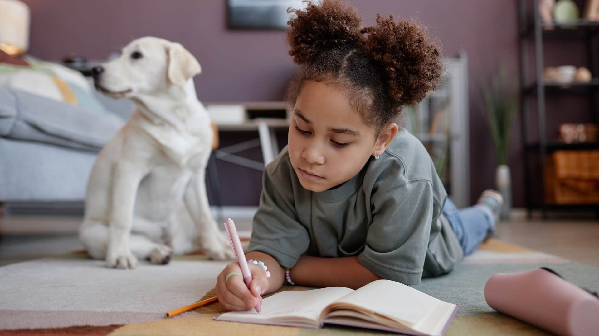 little girl doing homework next to her dog
