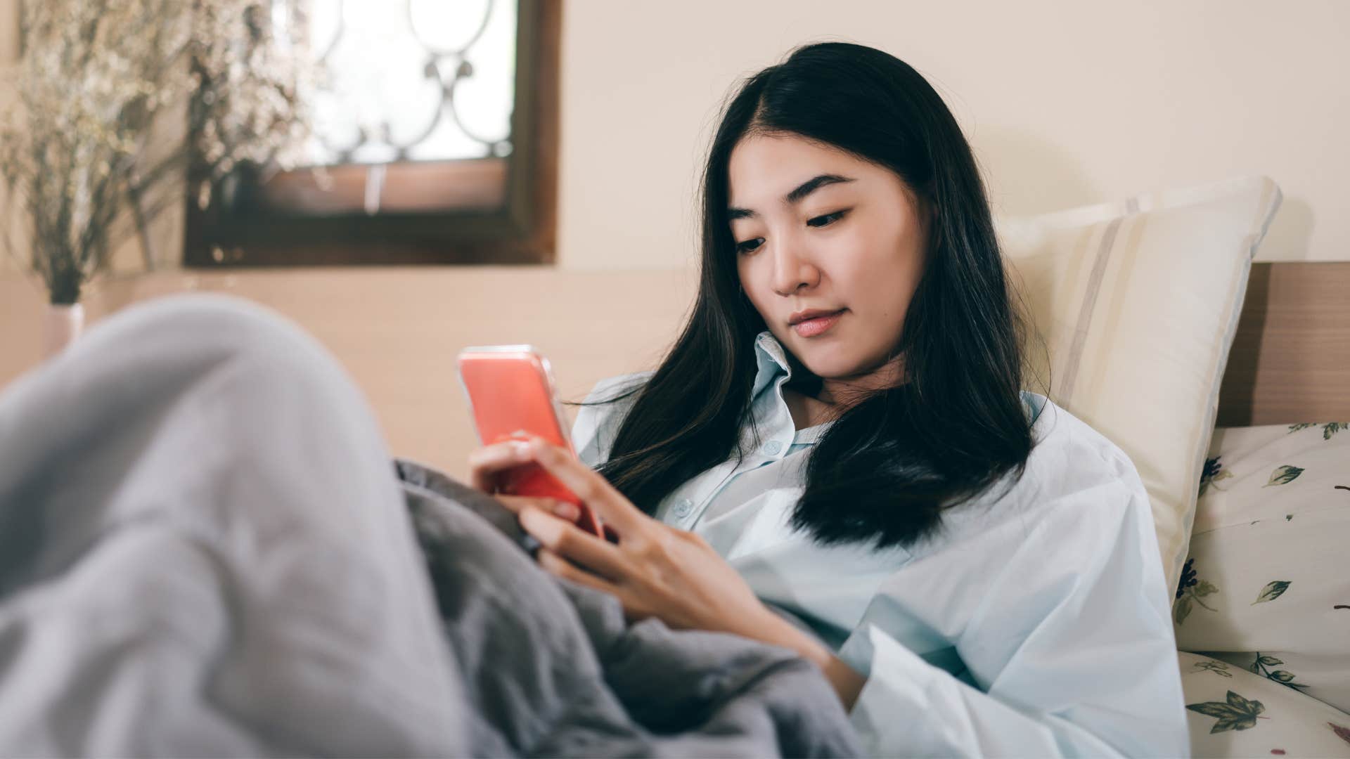 woman texting on phone as she lays in bed being an introvert