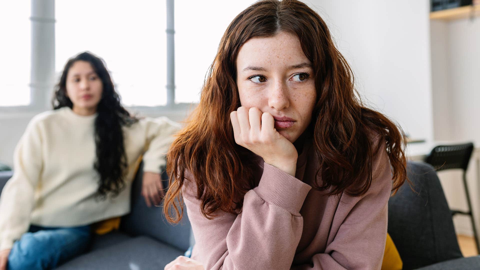 upset woman facing away from friend on couch