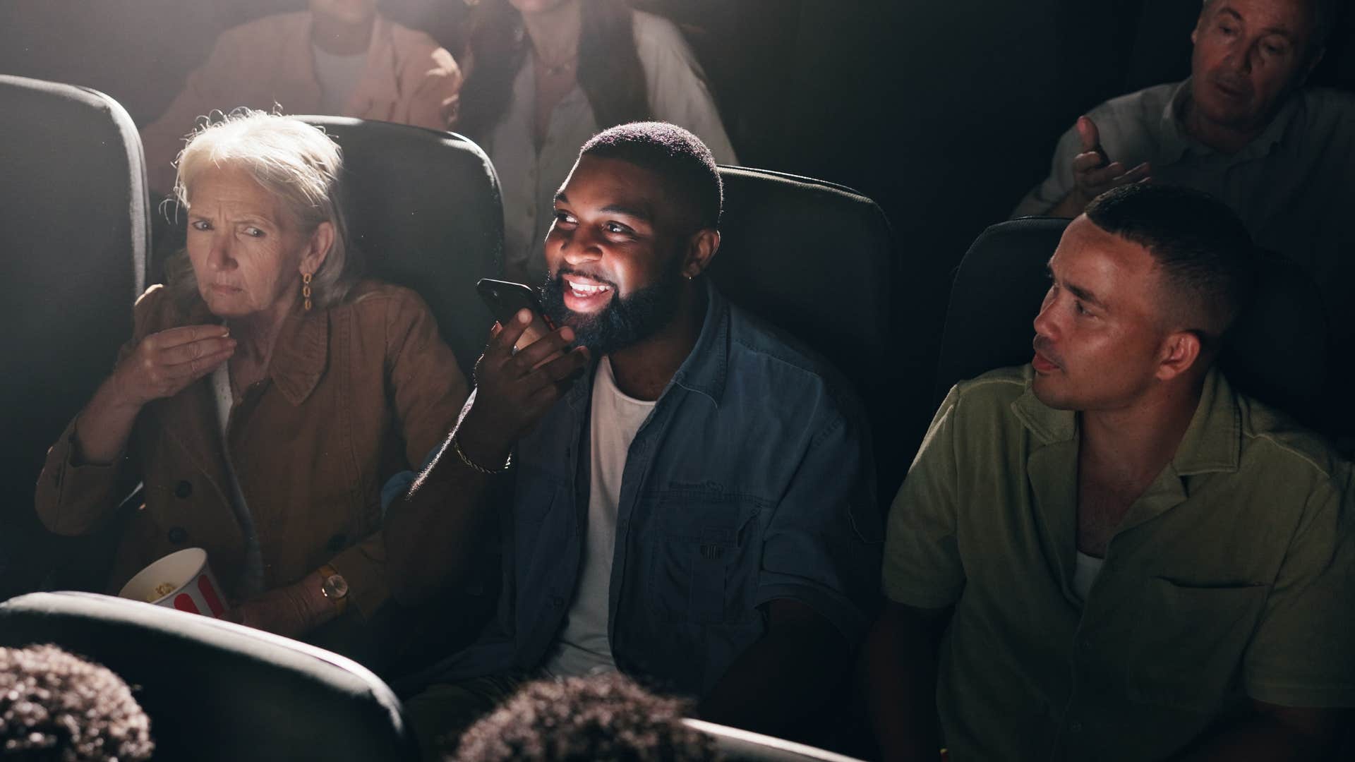 man talking on speakerphone in crowded movie theater