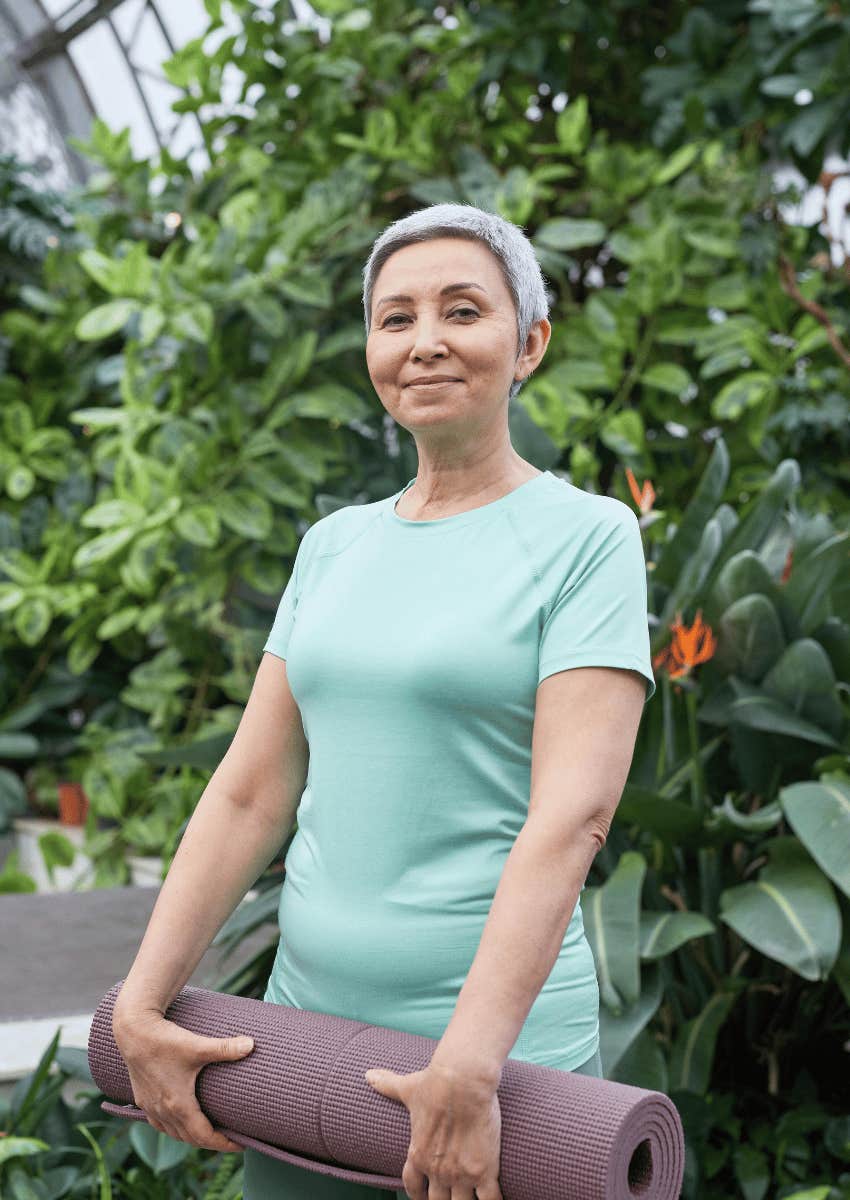 smiling older woman holding a yoga mat