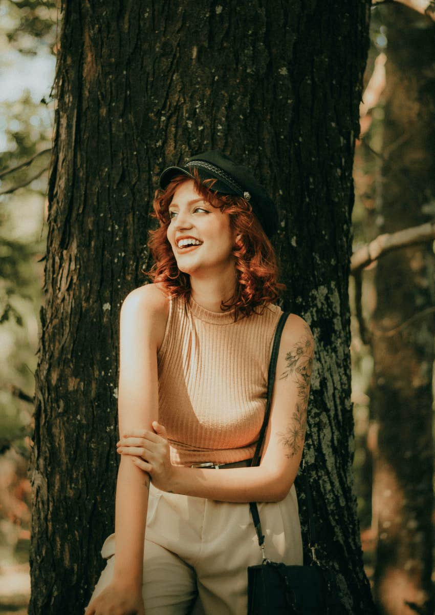 smiling young woman posing against a tree