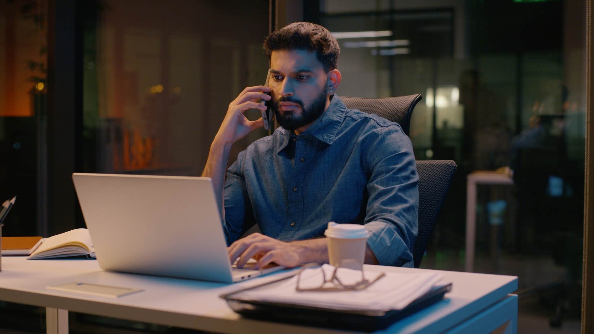 man in dark blue shirt working at strange hours as he's on the phone in office