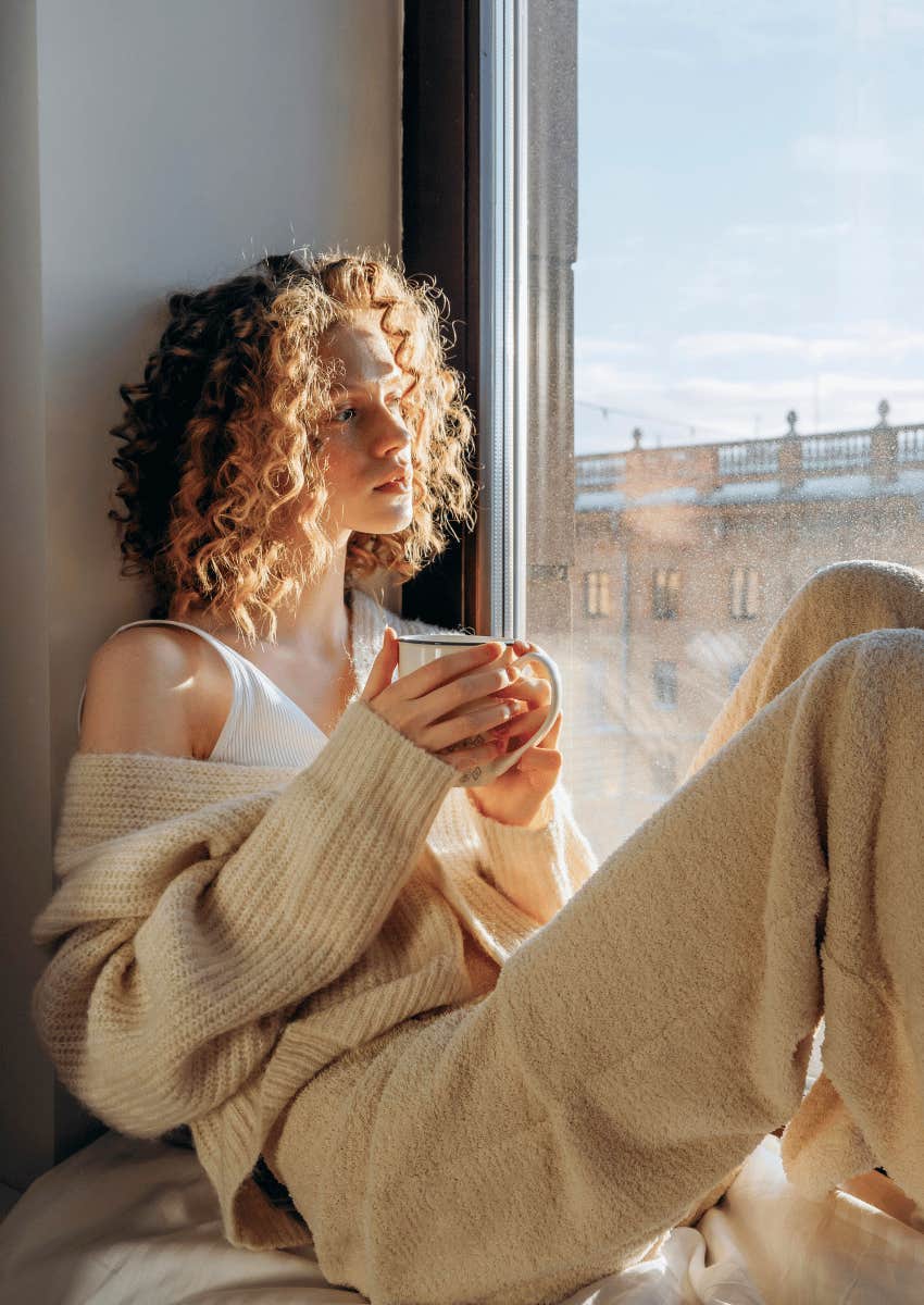 thoughtful curly haired woman looking out of window