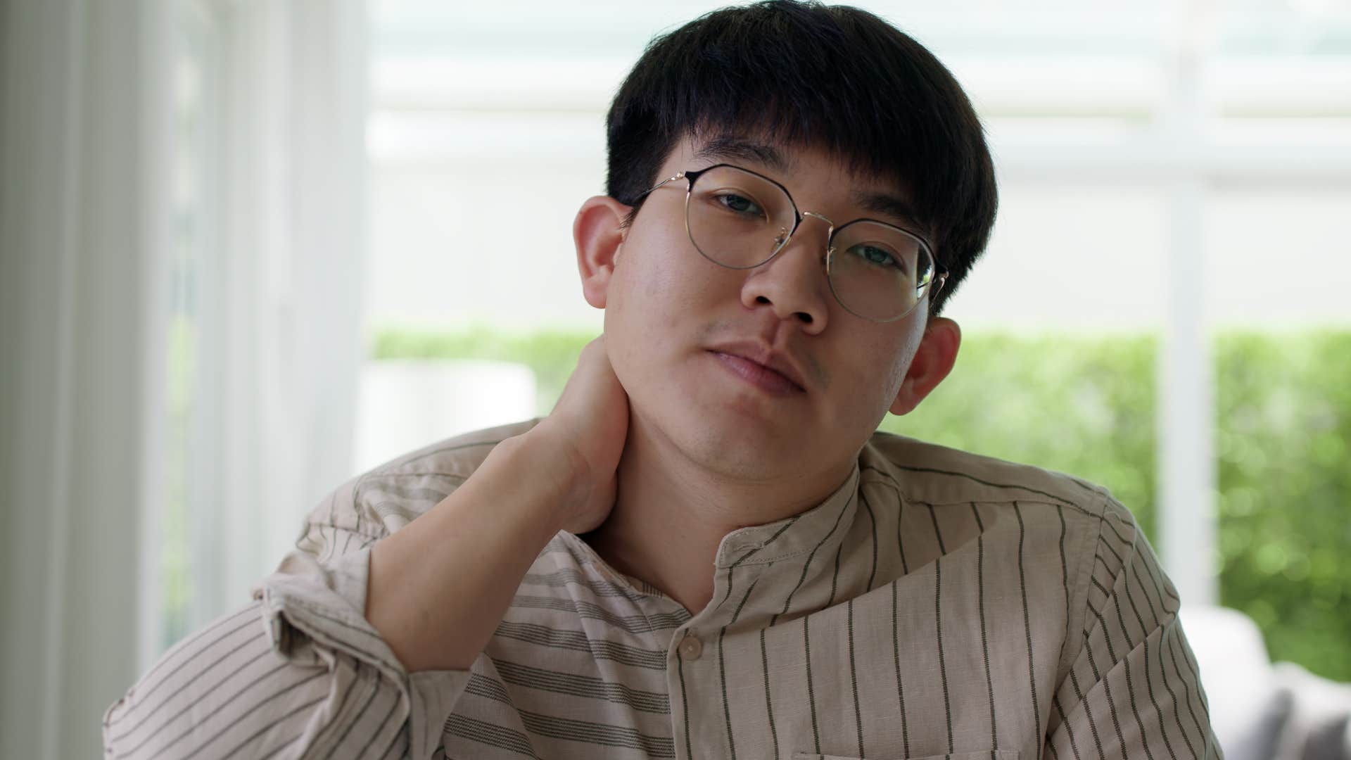 Man who overshares holding his neck at home.