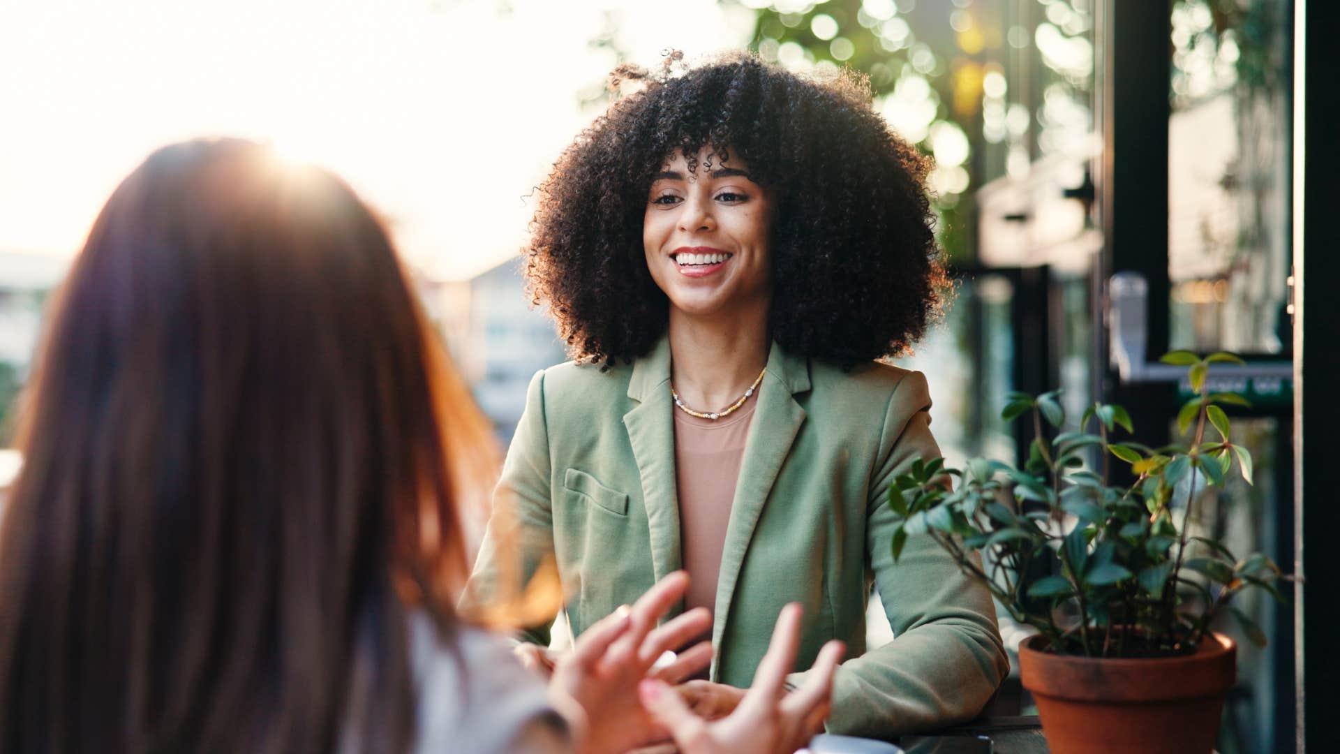 woman listening to friend speak while sitting outside at cafe