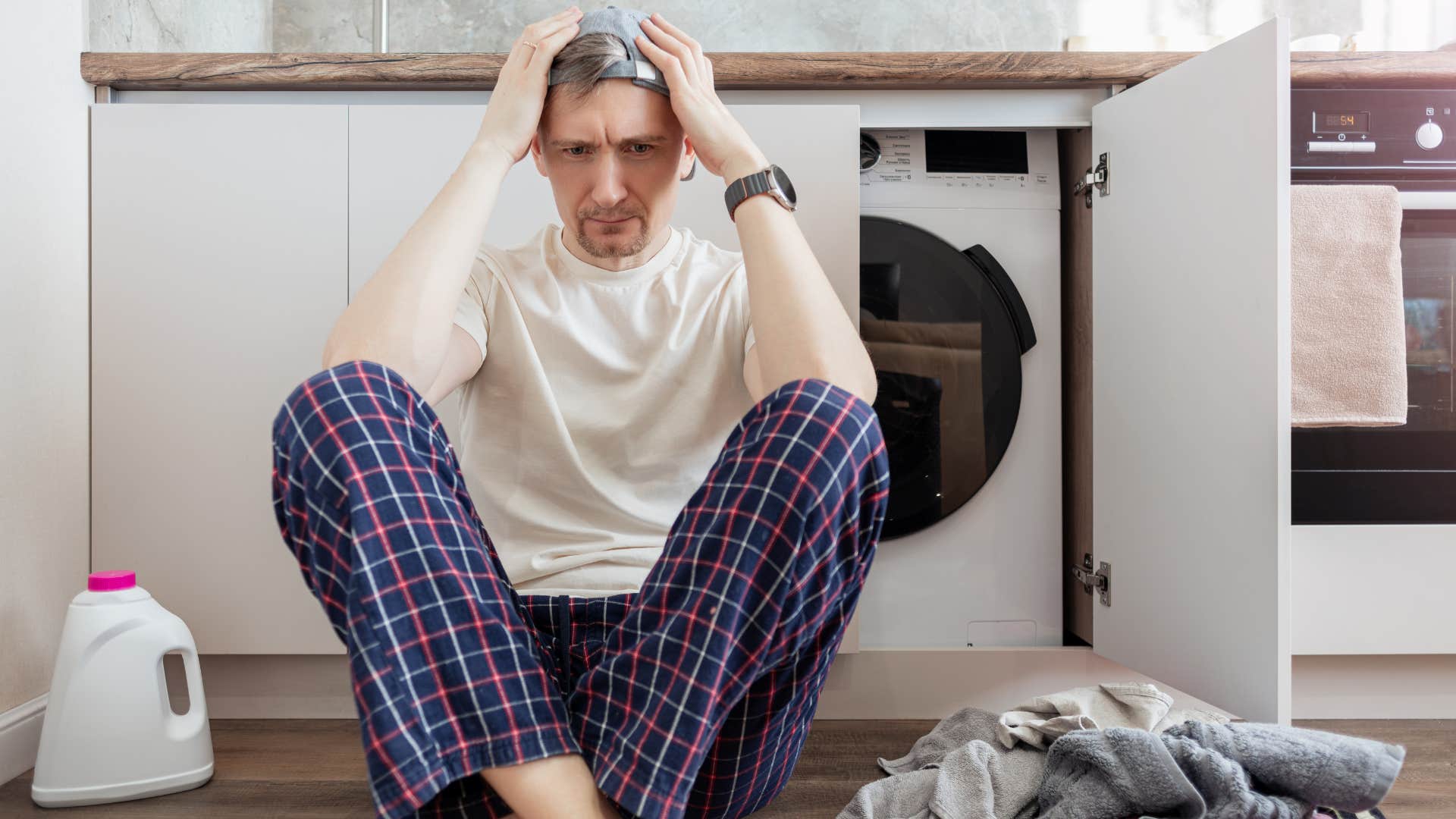 stressed man sitting in front of washing machine with pile of laundry