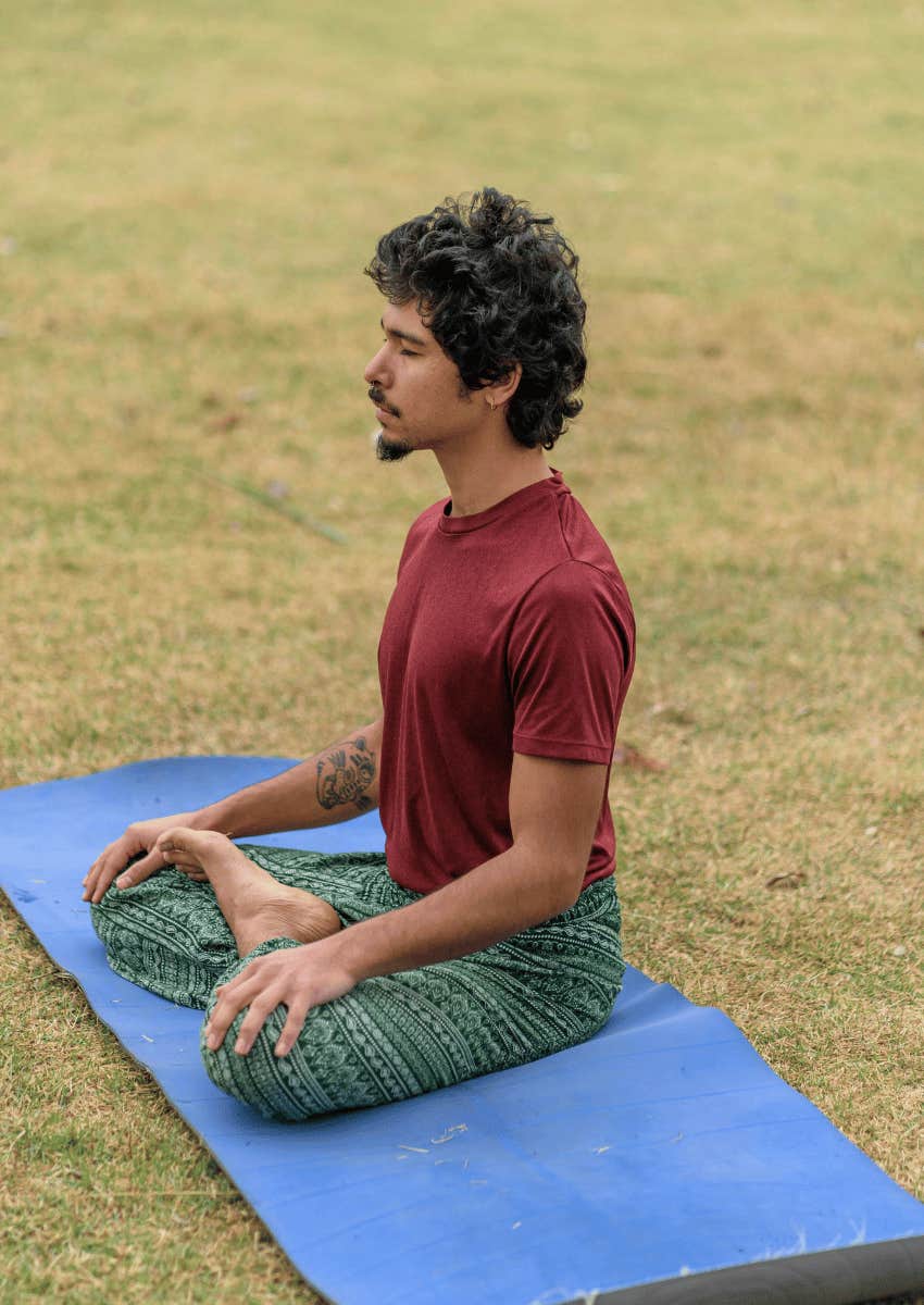 young man practicing self care by meditating outdoors