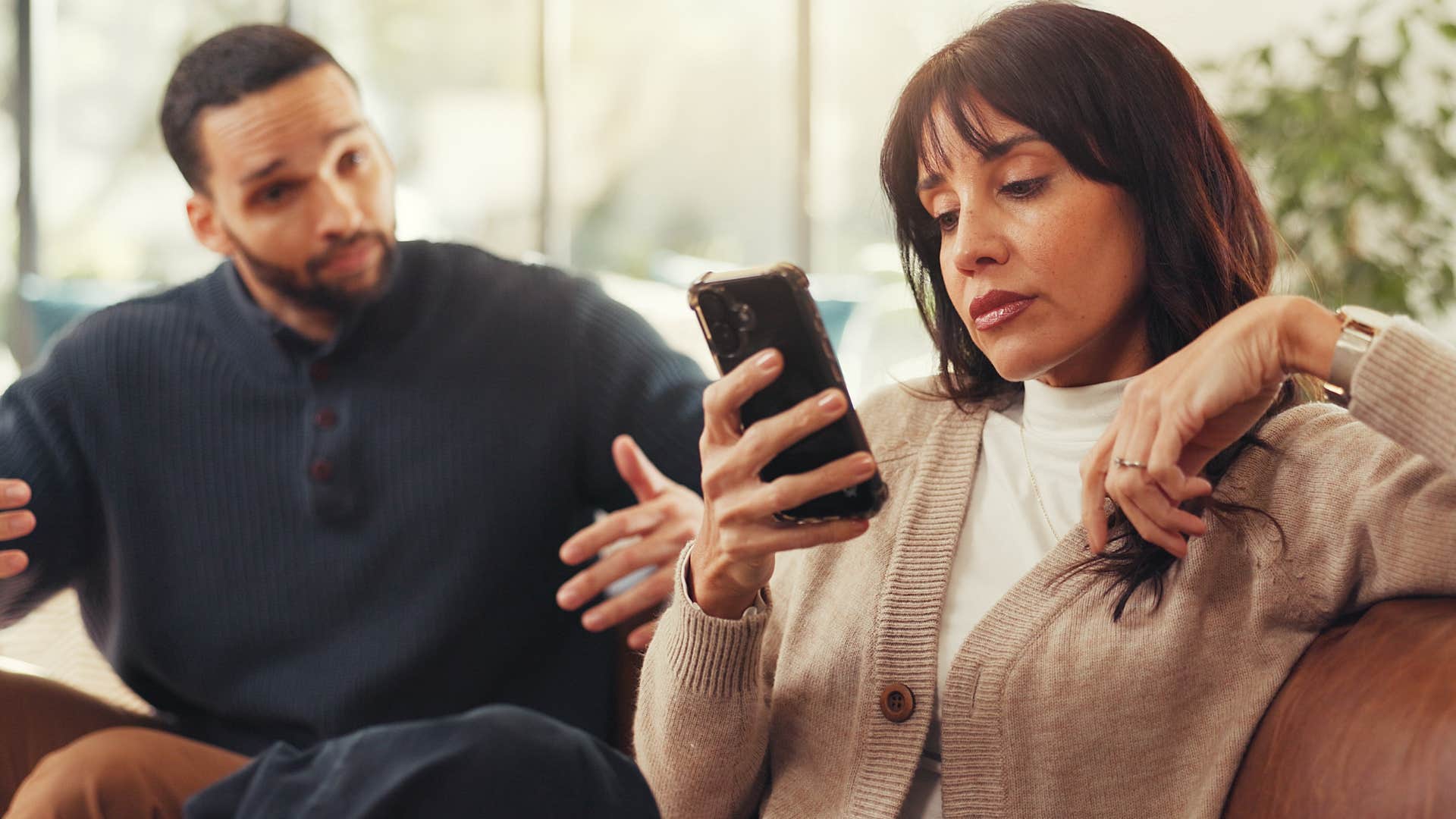 woman zoning out looking at phone while husband tries to talk to her