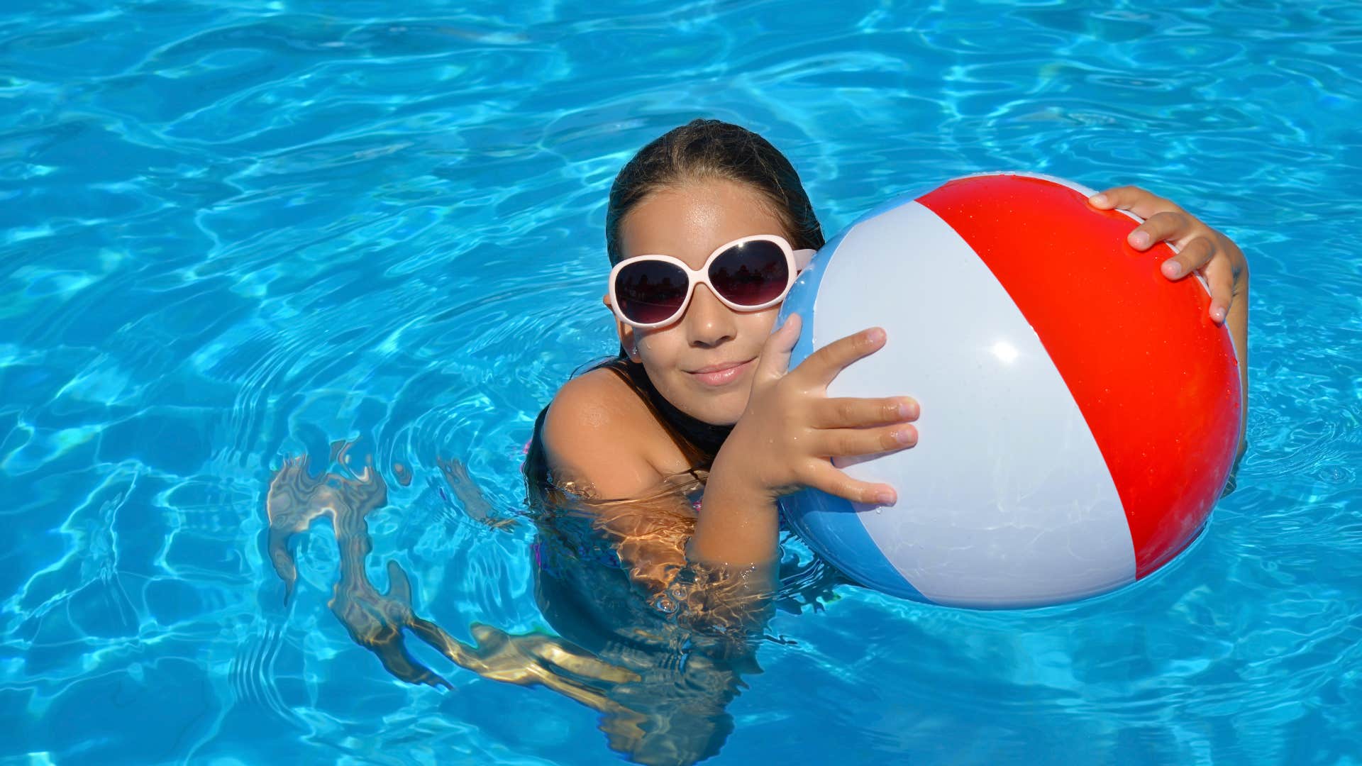 little girl in swimming pool with beach ball after eating