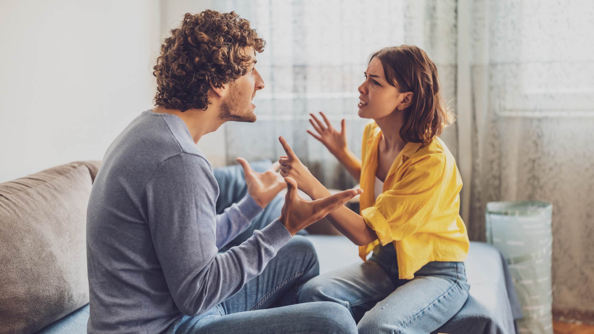 man in gray telling woman you're overreacting again as they argue on bed