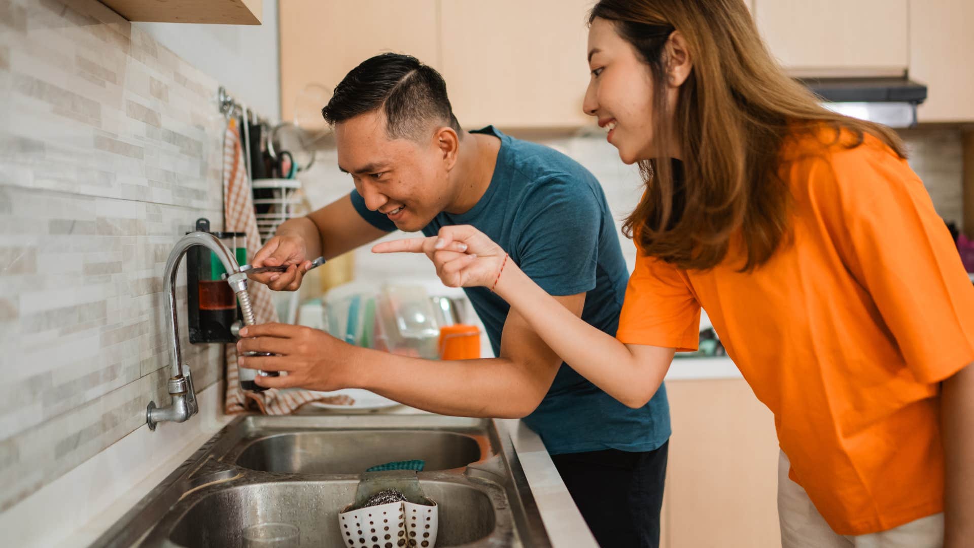 husband fixing sink with wife in kitchen