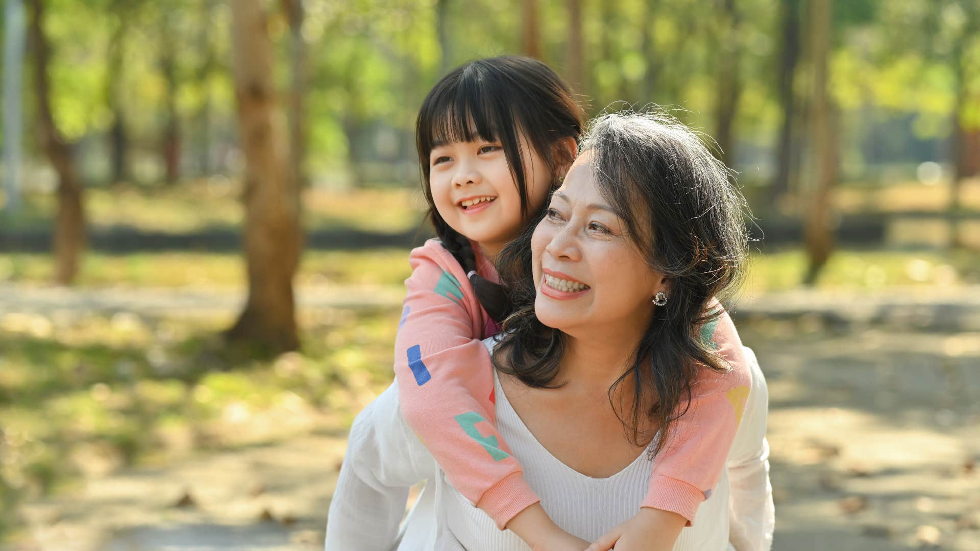 smiling middle age grandmother giving piggyback ride to granddaughter during walk in the park