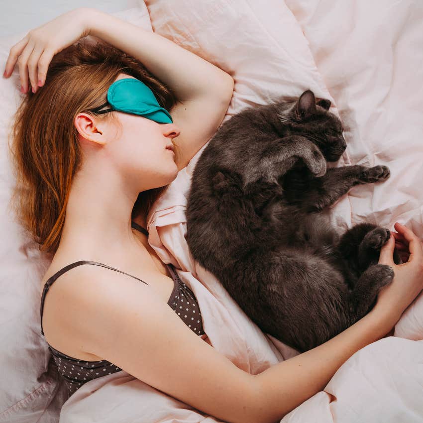 cat keeping sleeping woman warm in bed