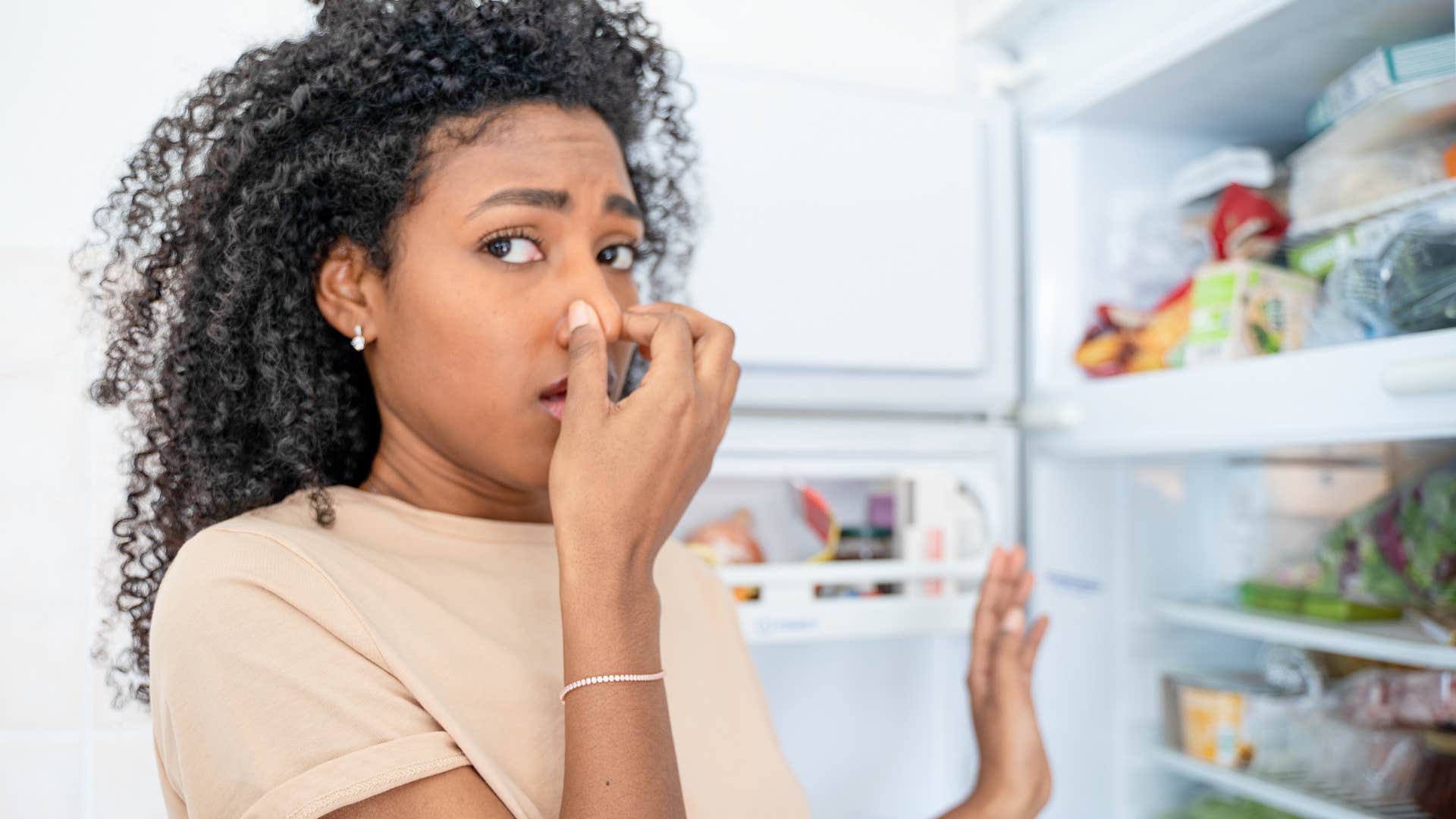 woman covering her nose grossed out at expired food in the fridge