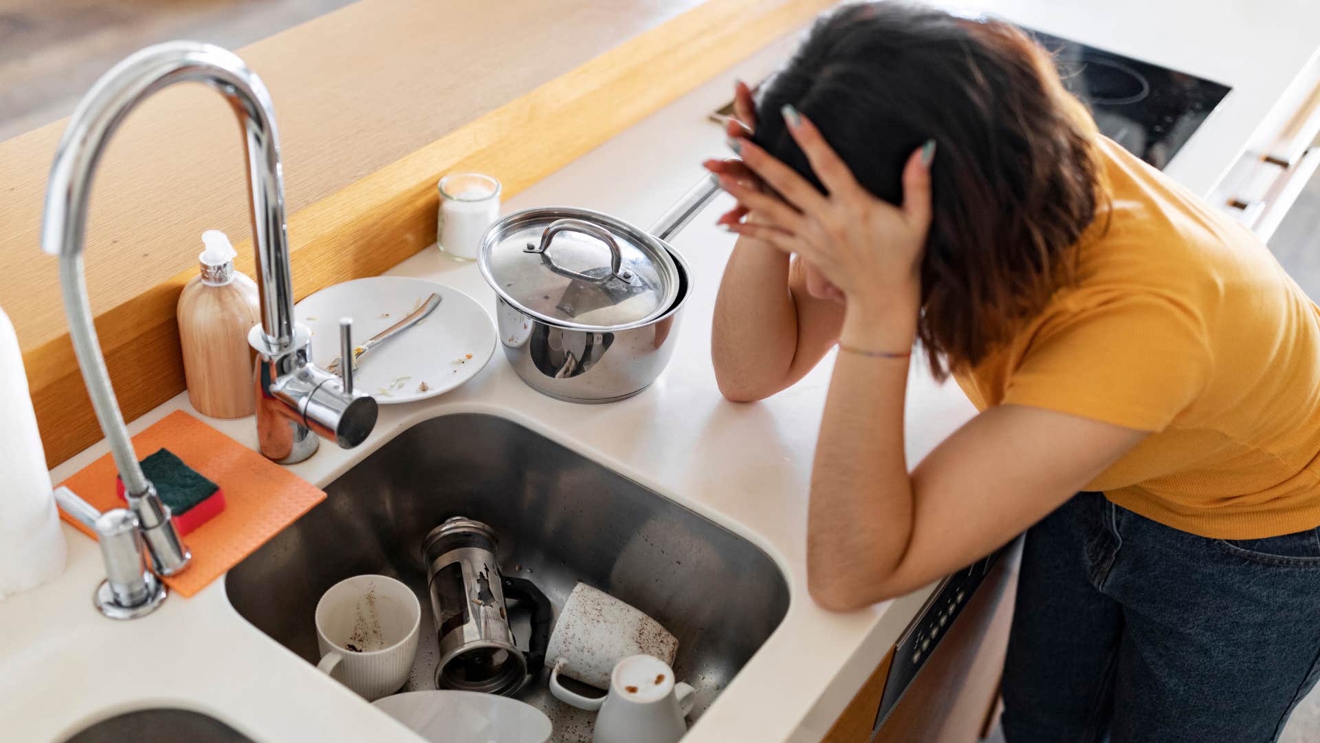 woman stressed out looking at full sink and splatter on backsplash