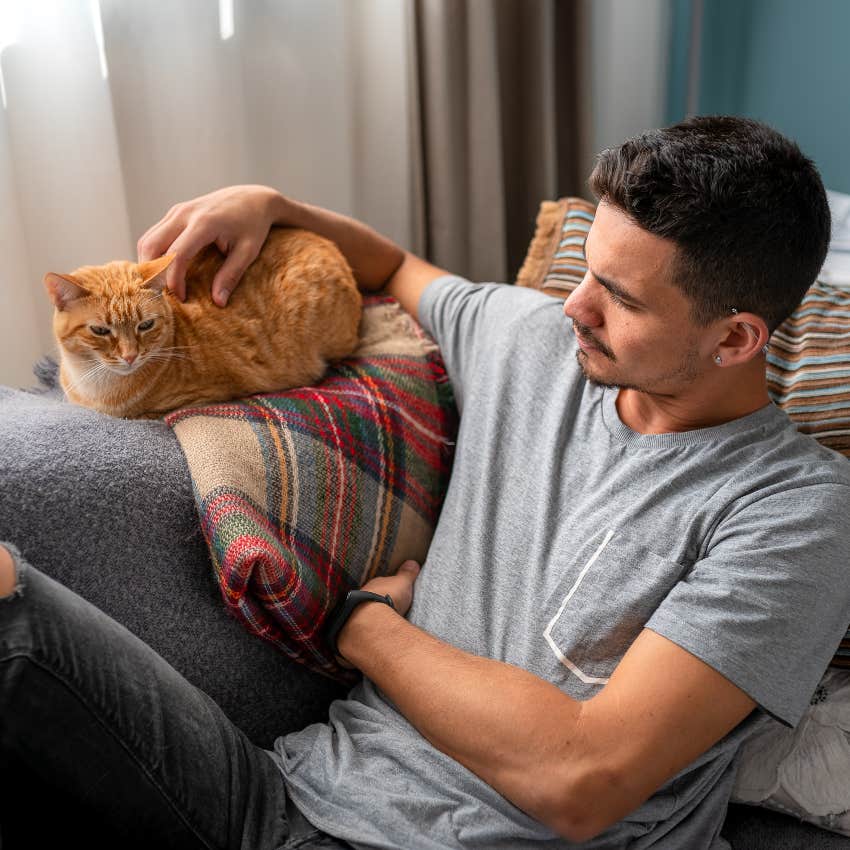 man petting purring cat on couch lowering his blood pressure