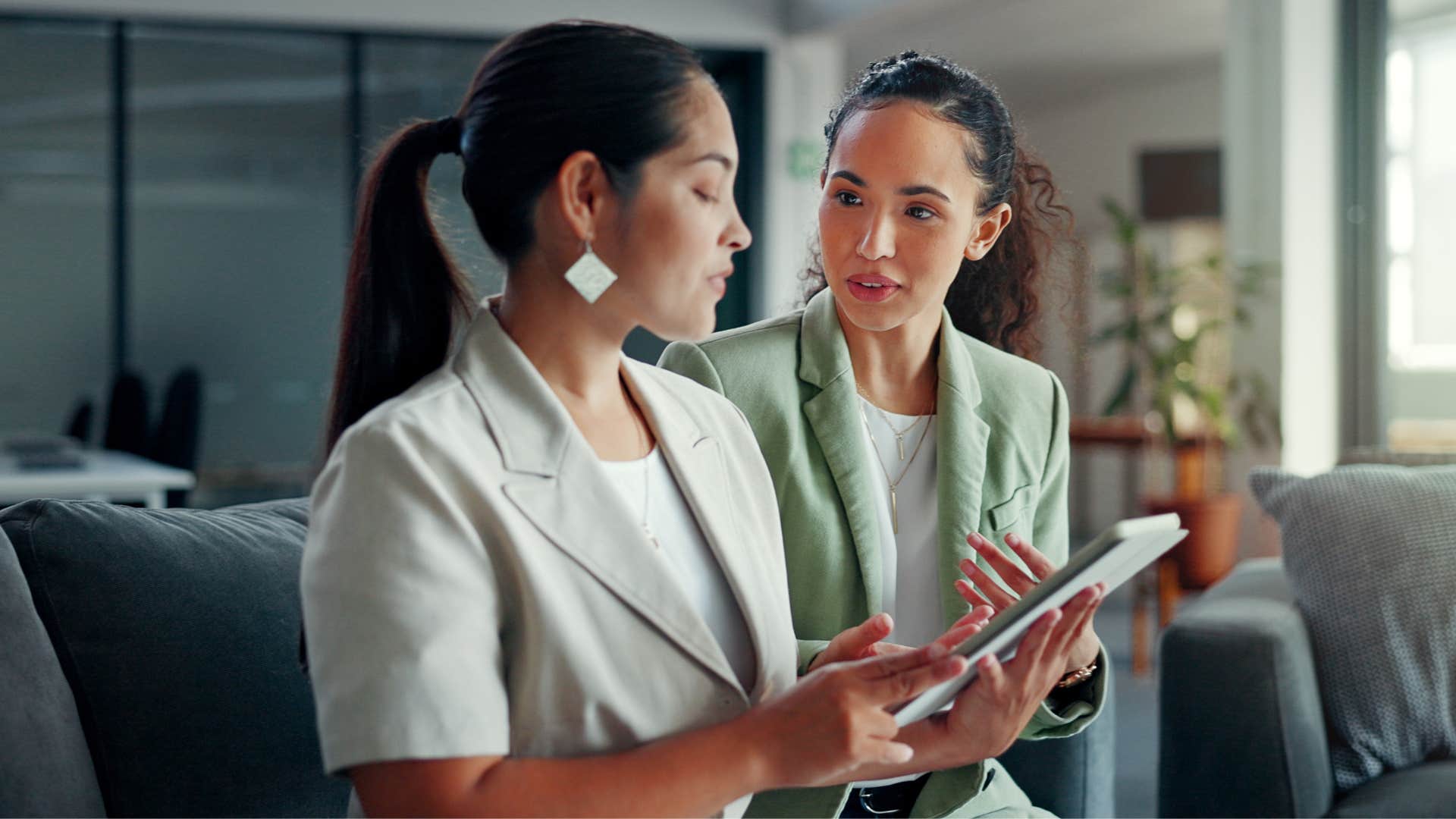 woman who doesn't try to impress anyone saying nevermind to coworker as coworker looks at tablet