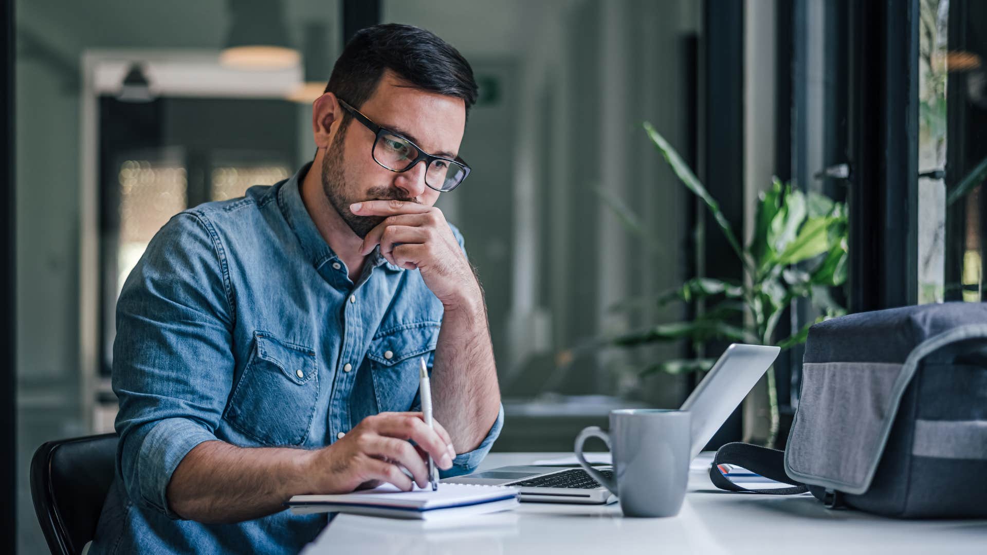 man in blue shirt thinking as he writes down notes