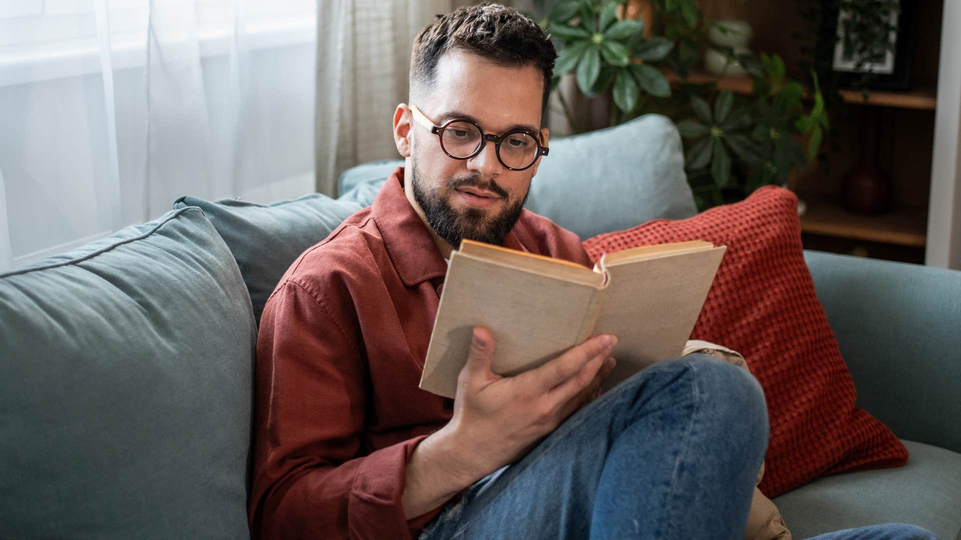 Man who's comfortable with boredom reading on his couch