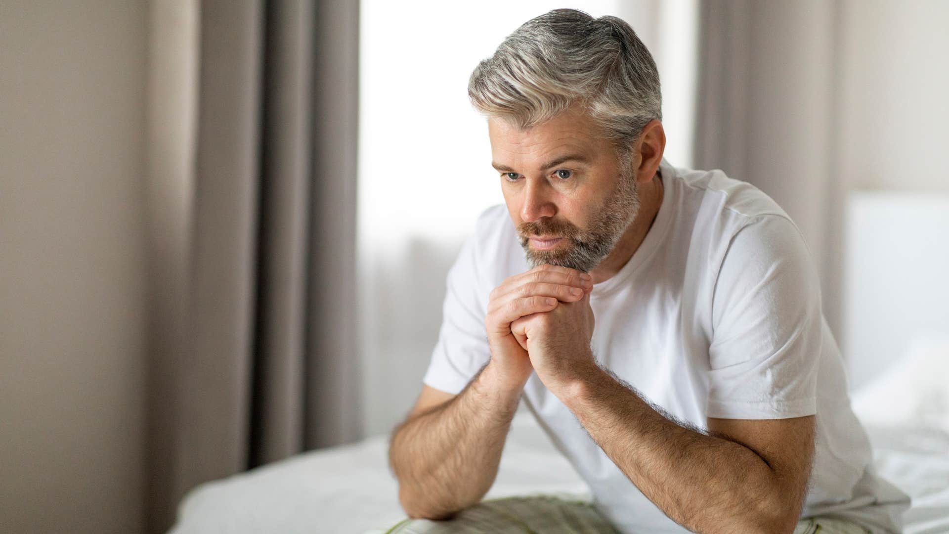self-aware man sitting on edge of bed thinking