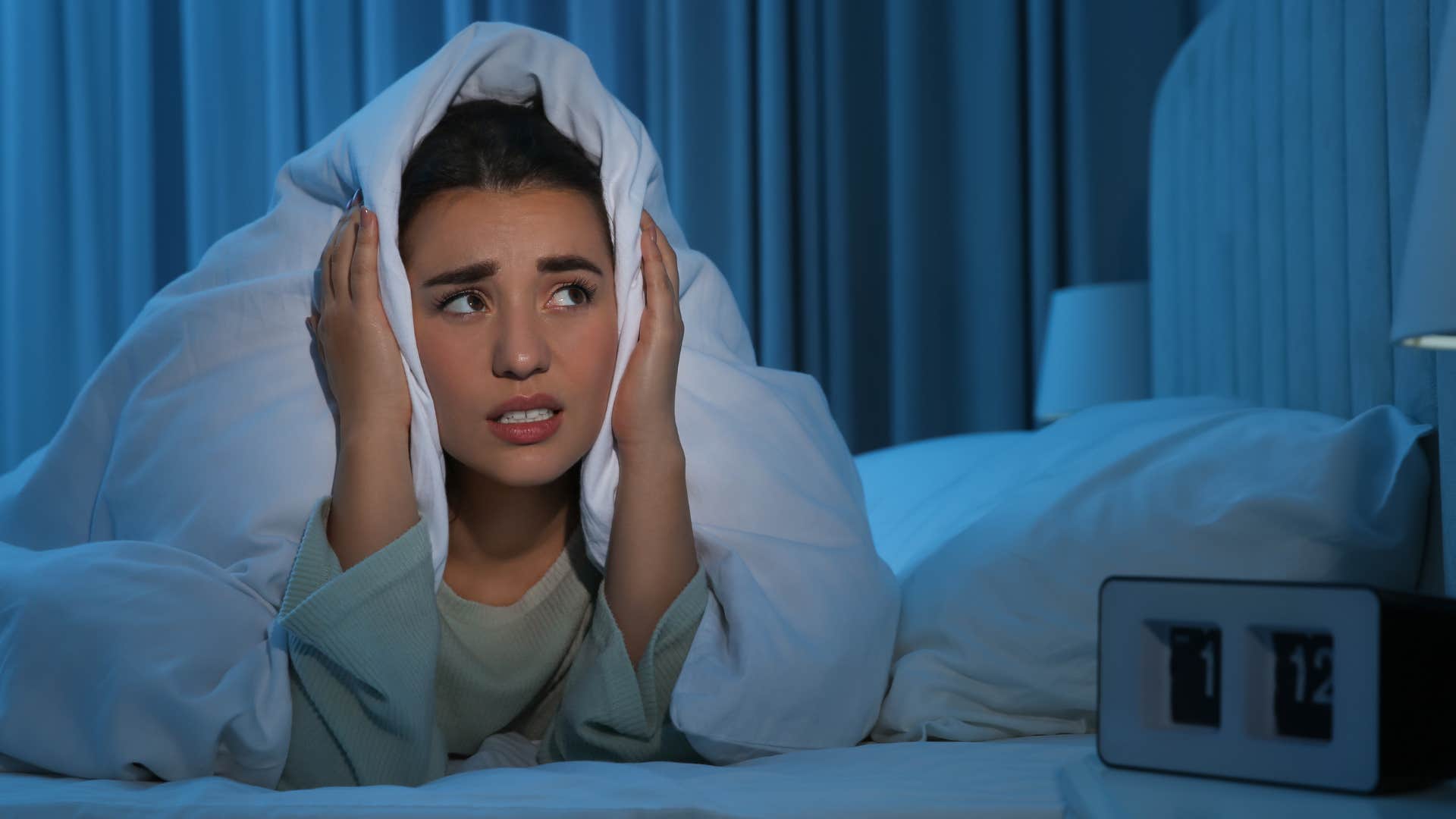 overthinking woman looking scared in her bed at night