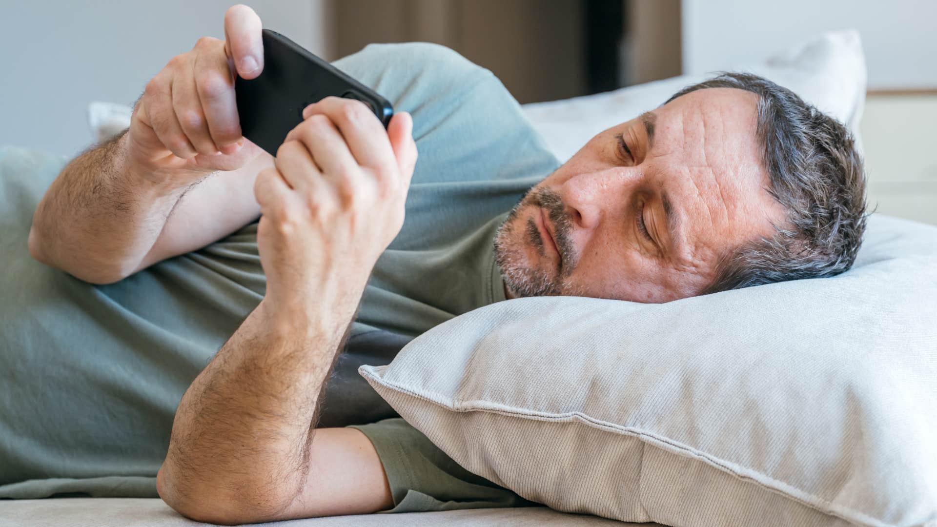 man laying in bed procrastinating personal tasks on his phone
