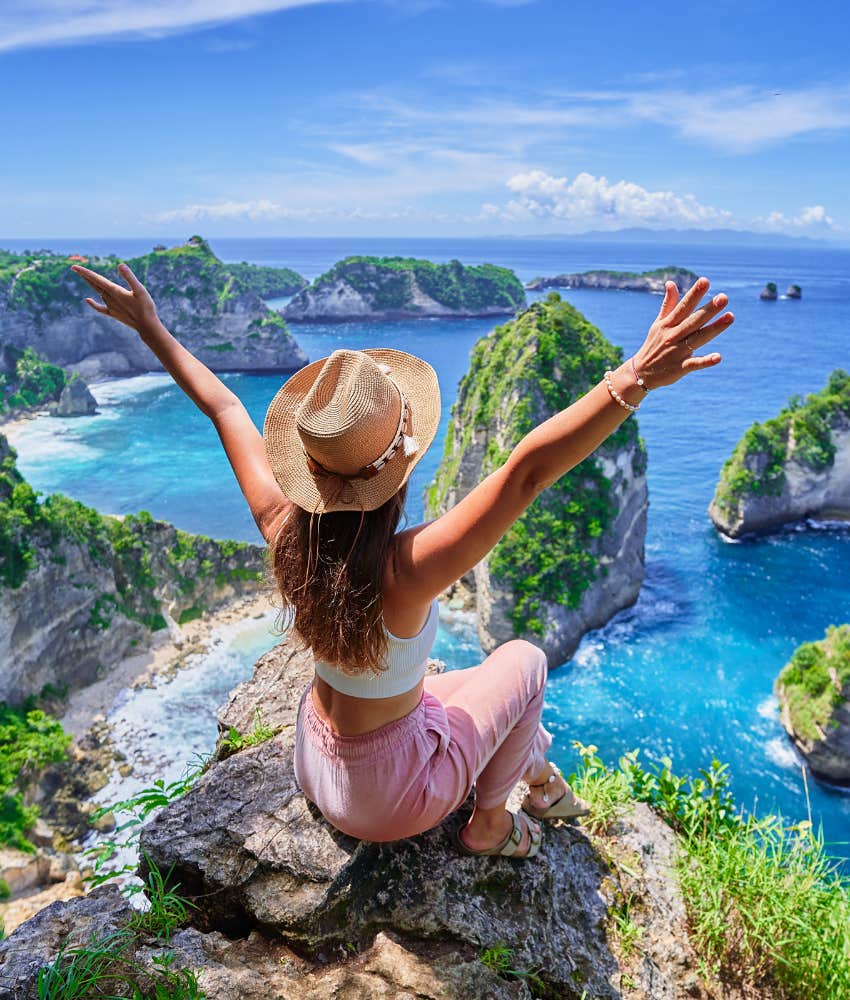 Excited traveler sits on cliff above ocean showing curiousity