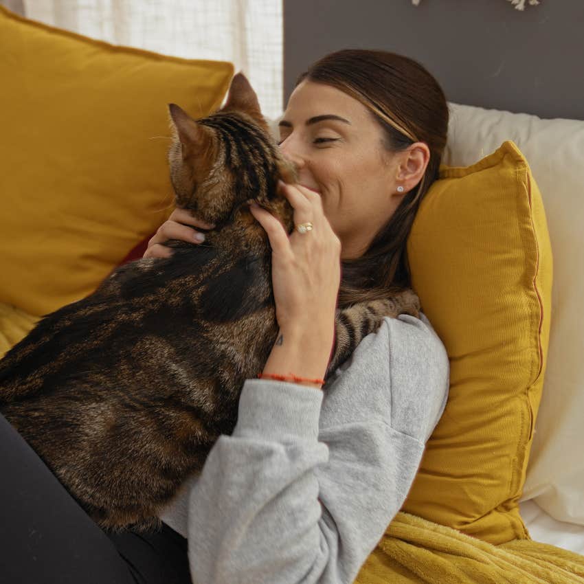 woman laying with purring cat on bed