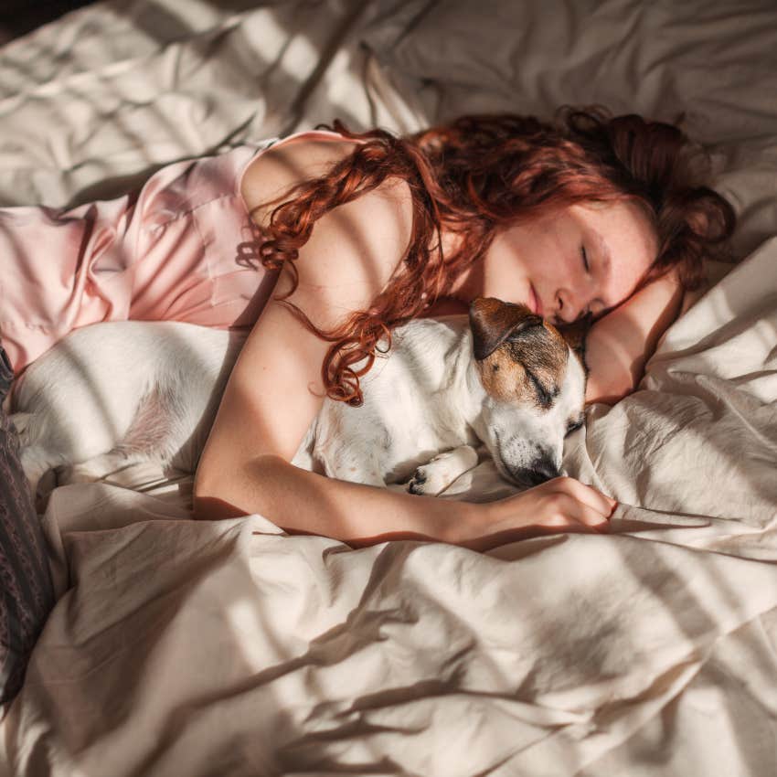woman comforted by her dog sleeping in bed with her