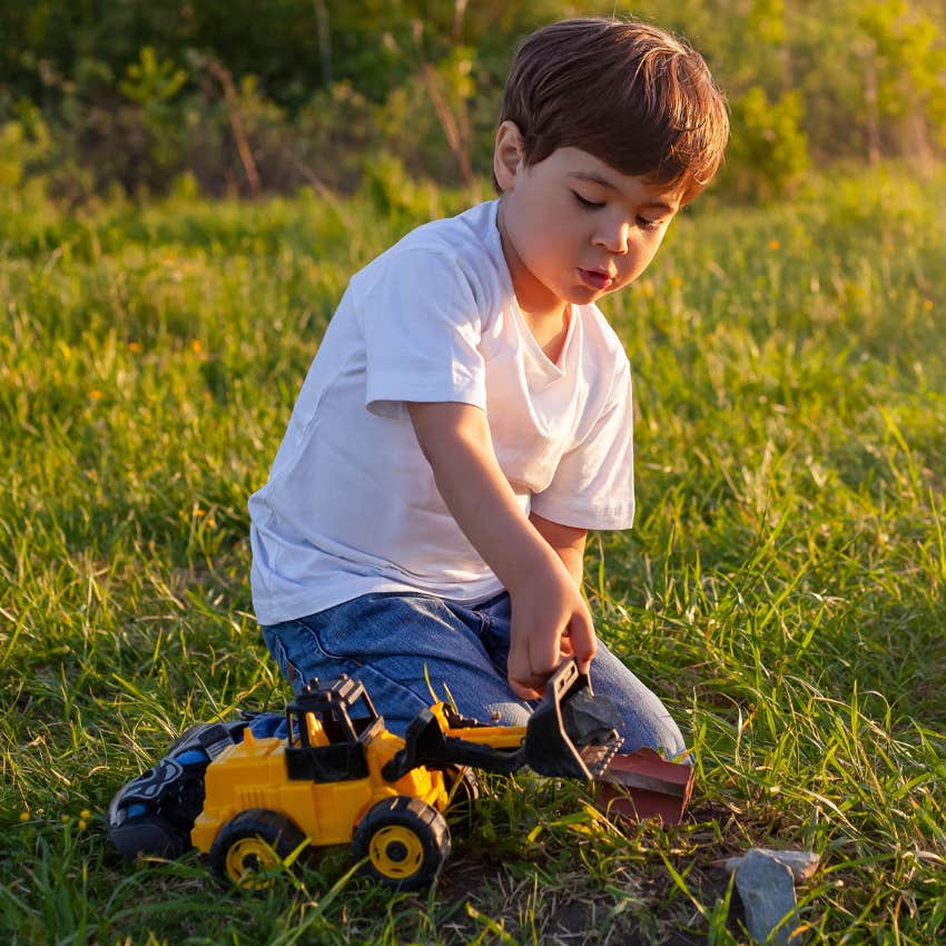 Little boy who plays outside alone sitting in the grass