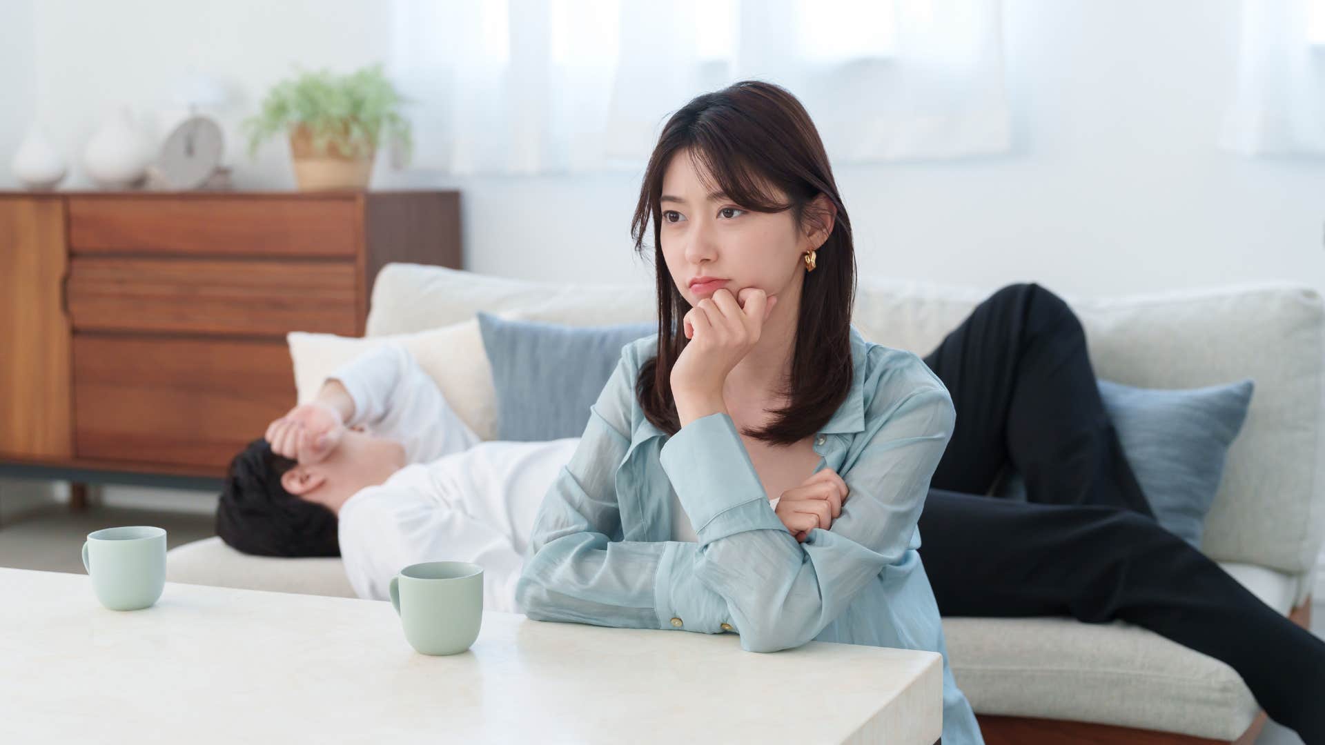 Unhappy person thinks while partner sleeps on couch showing settled love