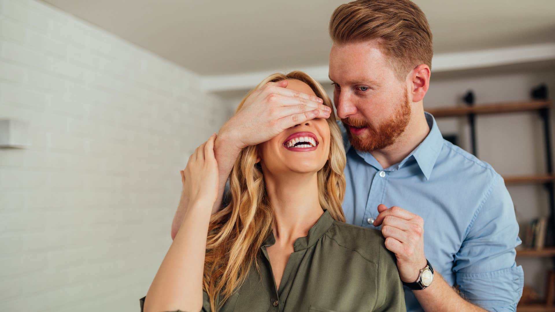 man celebrating his wife earnestly covering her eyes playfully