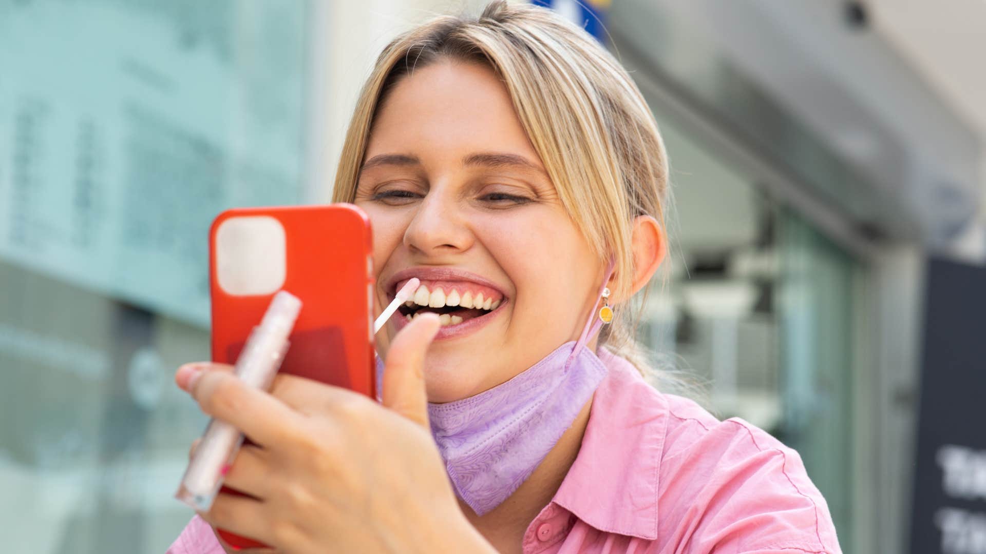 Self-aware woman putting on lip gloss outside.