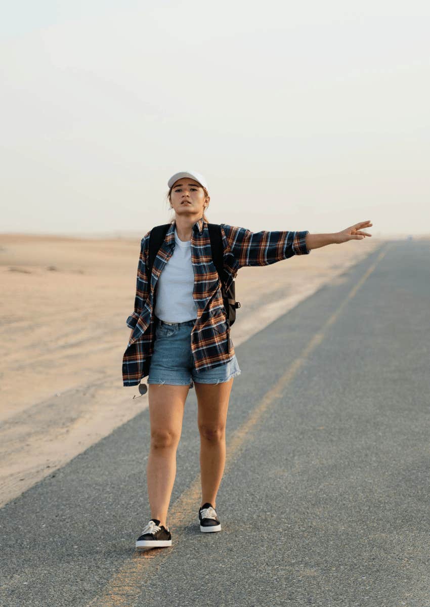 young woman in a flannel hitchhiking on a deserted road