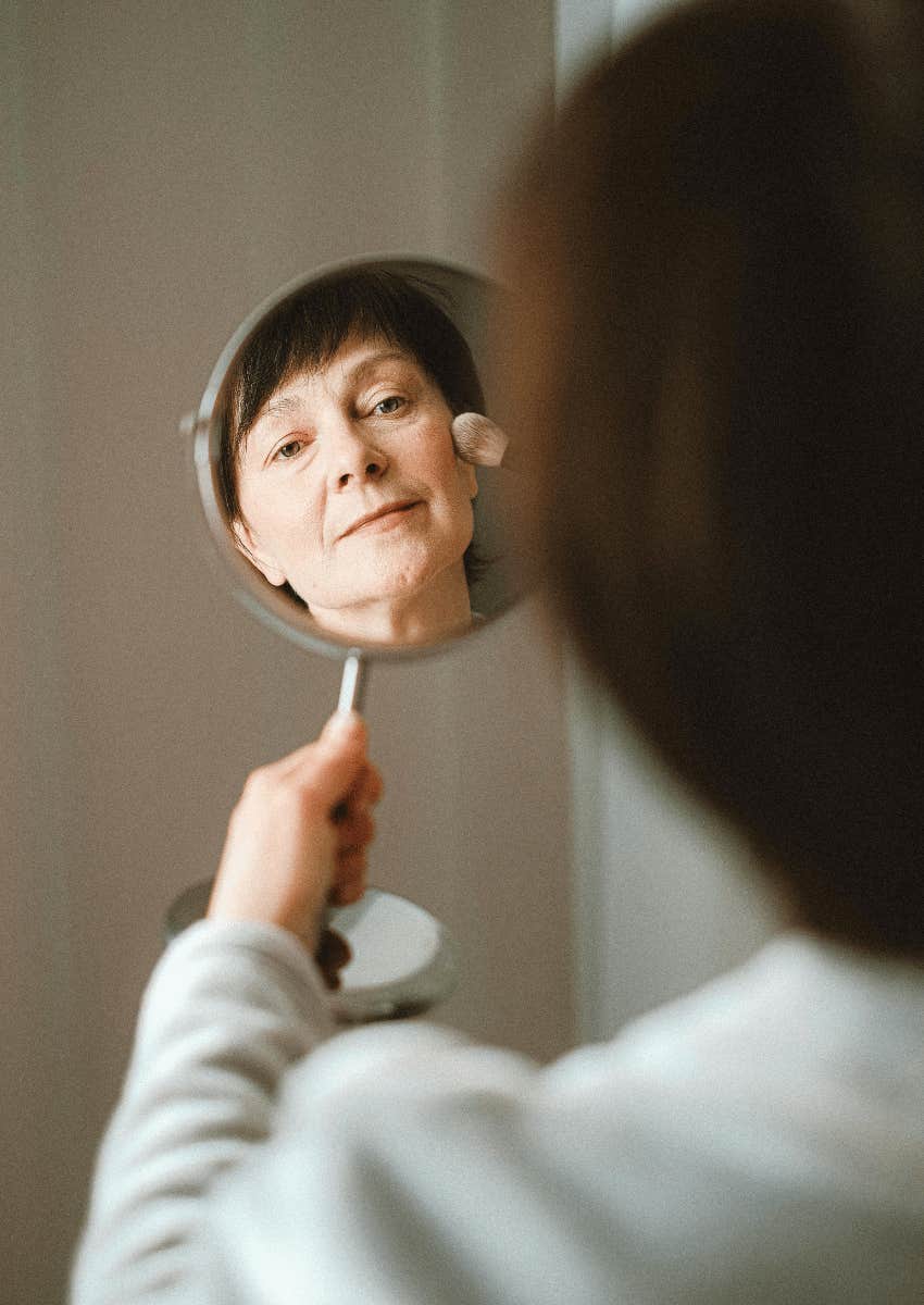aging middle aged woman looking at her reflection in a mirror