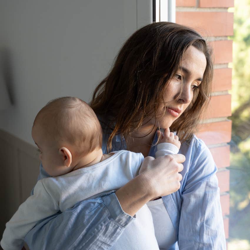 serious mom holding baby looking out window