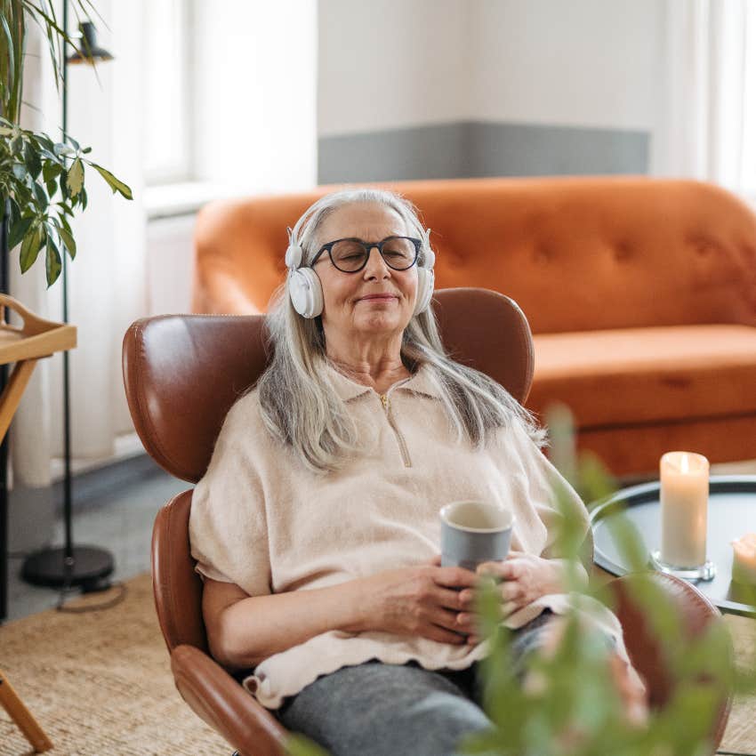 older woman listening to music while relaxing in chair with mug