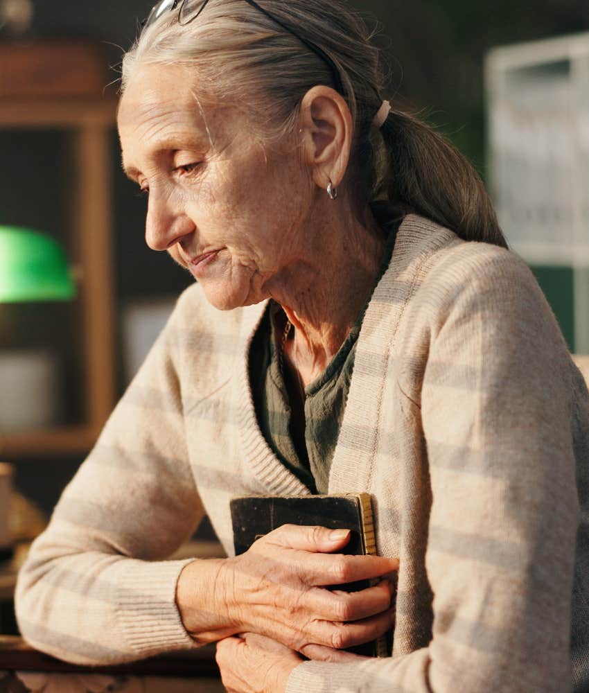 sad elderly person clutches notebook to chest showing worked too hard