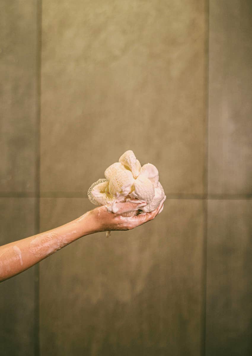 hand holding a soapy loofa in the shower