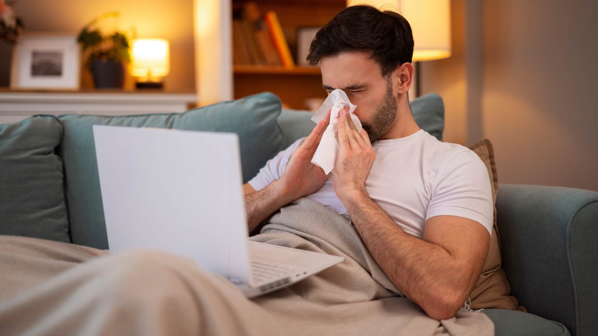 man blowing his nose feeling sick in bed